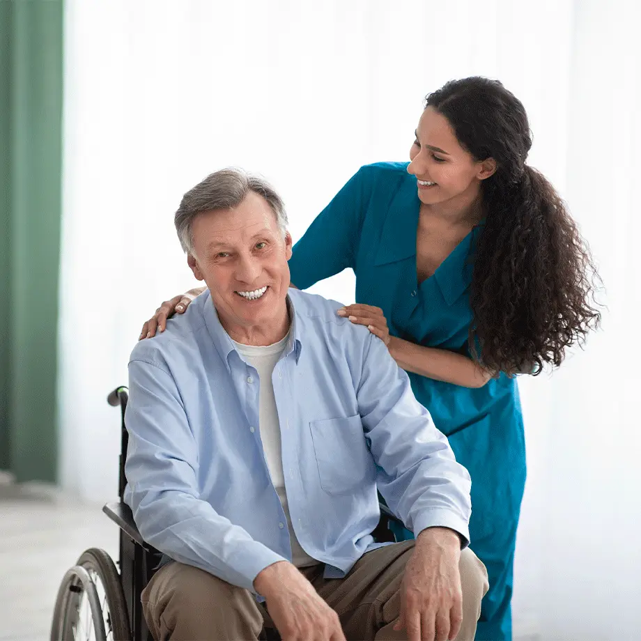 Elderly man in a wheelchair receiving NDIS disability support from a friendly NDIS support worker in a blue uniform, providing home care services in a bright and welcoming environment.