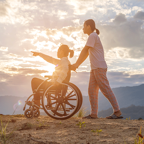 Support worker assisting a woman in a wheelchair outdoors at sunset, representing continence and disability support services in East Brisbane.