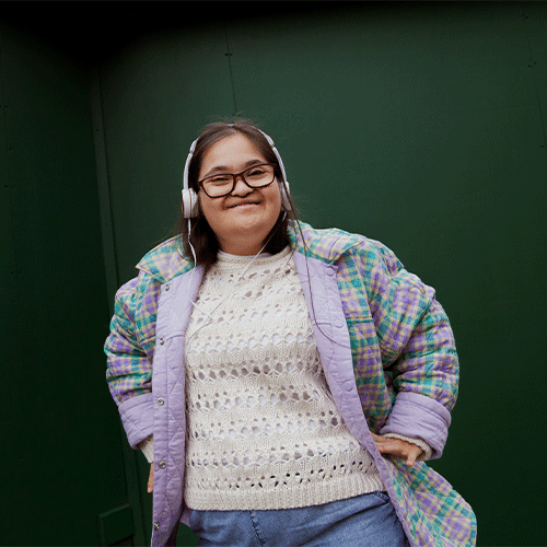 Young woman with Down syndrome smiling confidently, wearing headphones and a pastel plaid jacket, representing NDIS continence assessment clients in Craigieburn VIC.